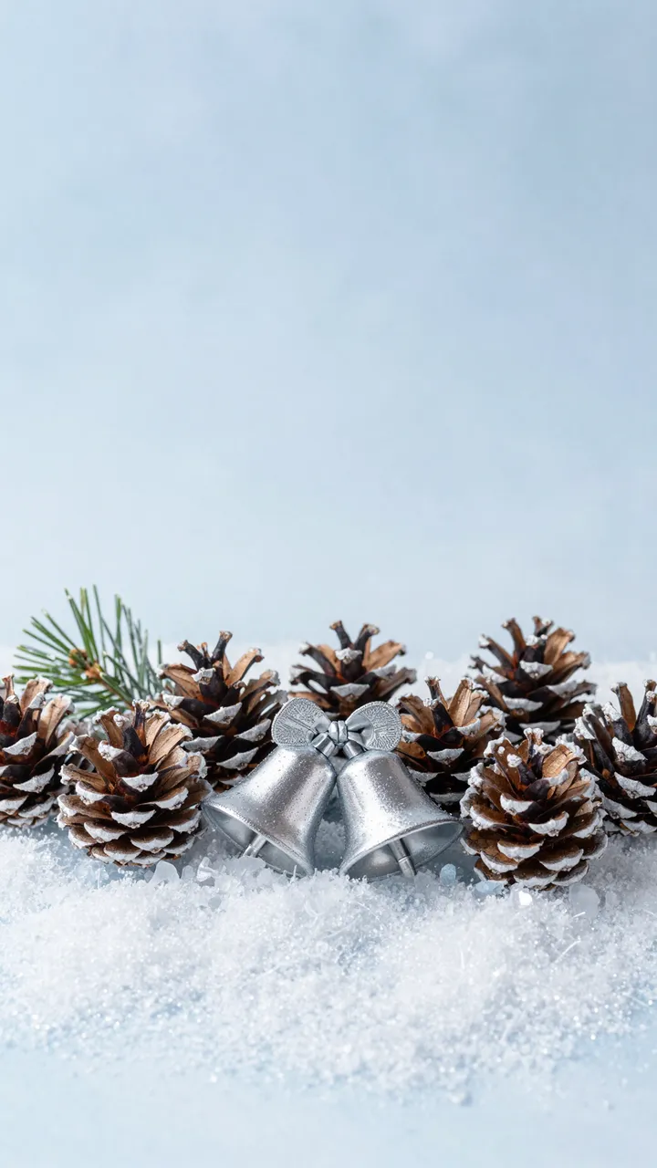 Frosted pinecones and silver bells rest on sparkling snow with empty icy blue copy space above