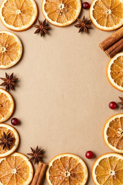 Top down flat lay of dried orange slices, star anise, cinnamon and cranberries framing empty kraft paper copy space
