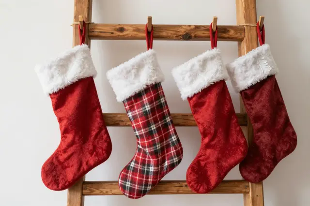 Four festive Christmas stockings hang from a rustic wooden ladder against a plain light wall