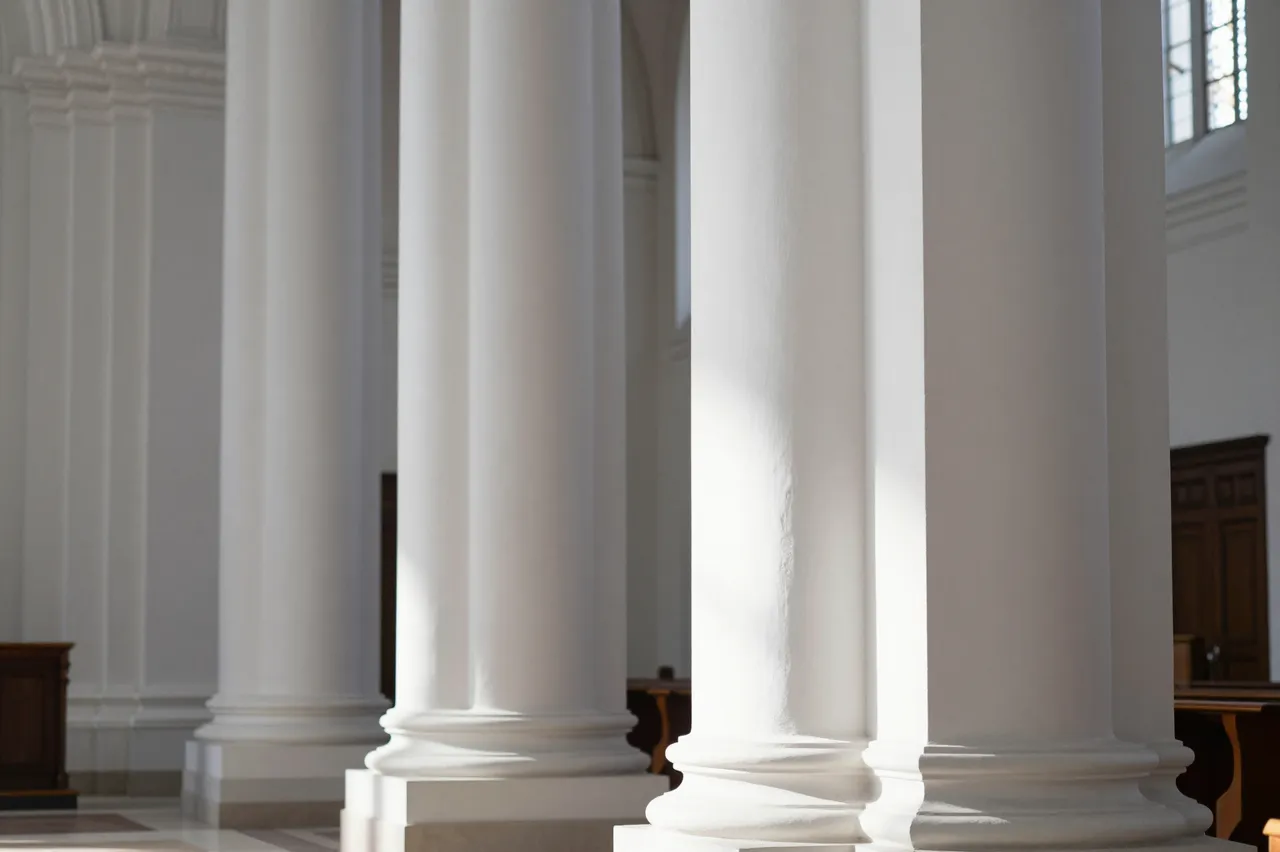 Tall smooth white columns inside a sunlit church interior with soft morning illumination