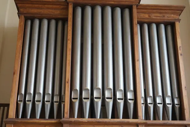 Close-up view of polished metal church organ pipes set within a wooden case under soft lighting