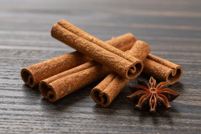 Dried cinnamon sticks arranged with a single star anise on a dark grained wooden table