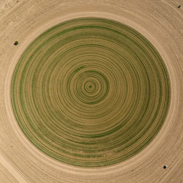 Top-down aerial view of concentric circular irrigated farmland surrounded by dry brown plain