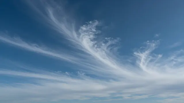 Wispy streaked cirrus clouds drift across a rich deep blue sky