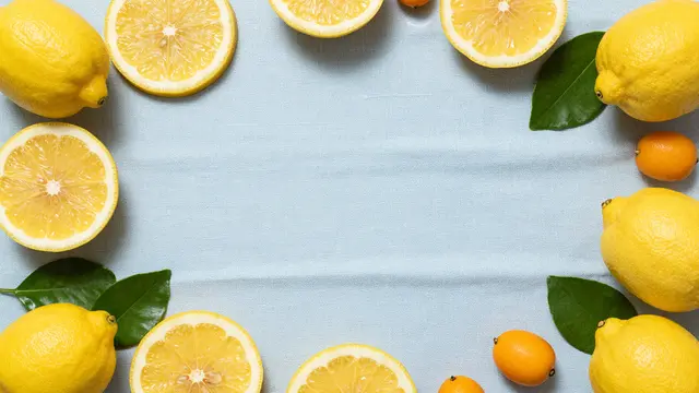 Overhead view of lemons, lemon slices, leaves and kumquats framing empty pale blue linen with bright summer lighting