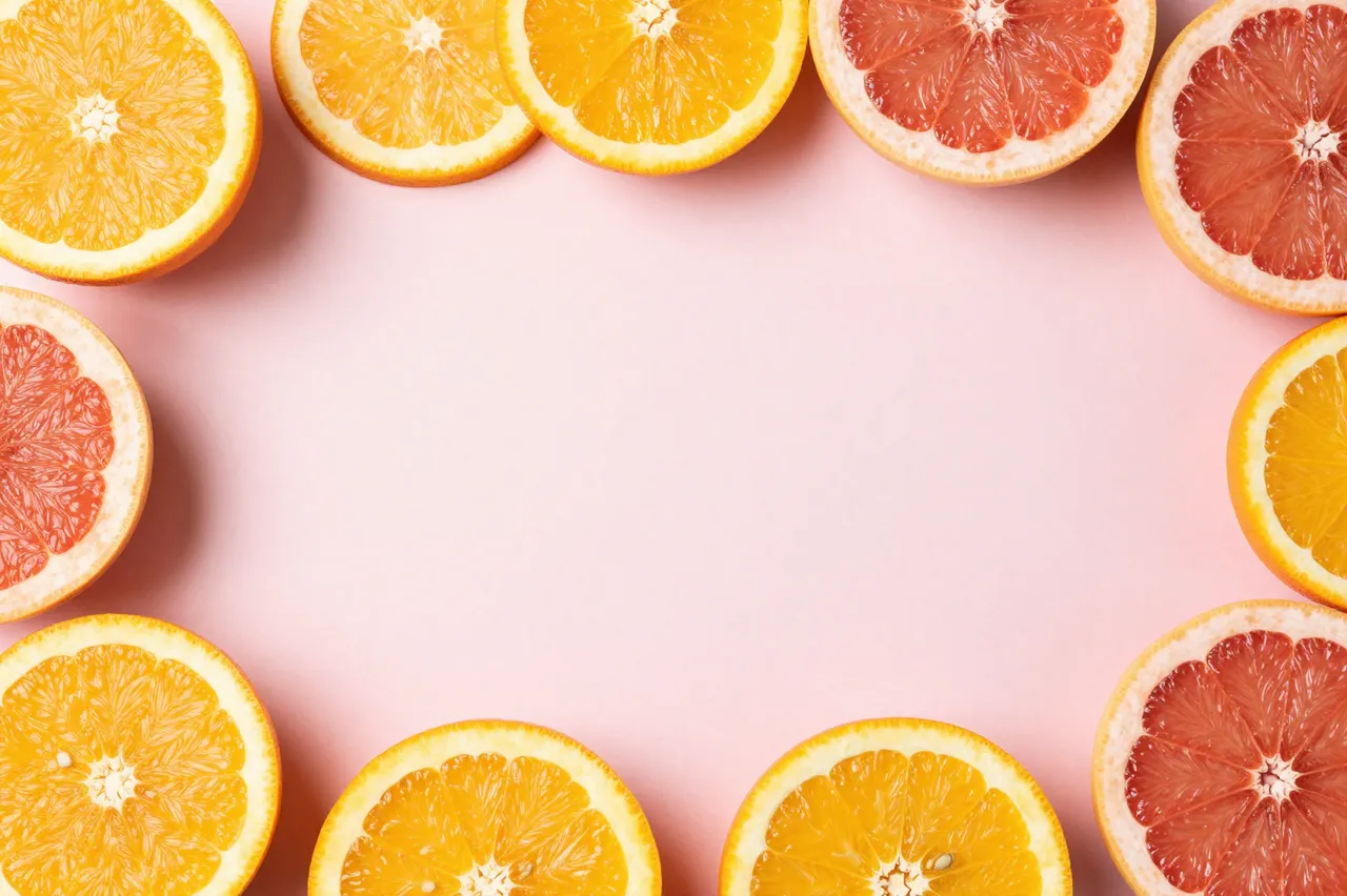 Halved orange and grapefruit slices frame an empty soft pastel pink center copy space.