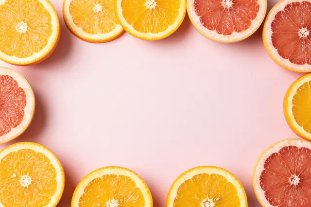 Halved orange and grapefruit slices frame an empty soft pastel pink center copy space.