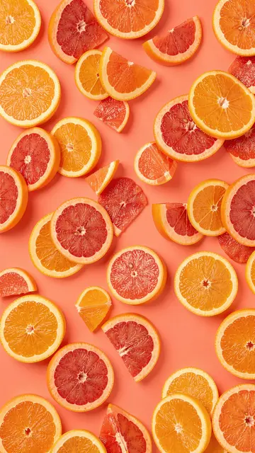 Scattered orange and grapefruit slices arranged across a solid warm coral background