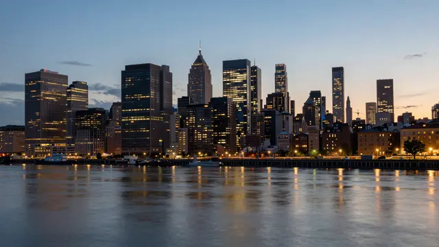 Illuminated downtown skyscraper skyline reflects in a calm river at twilight