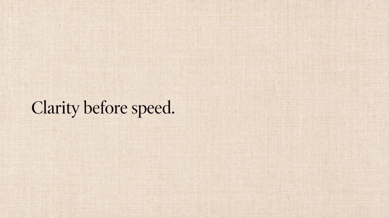 The text "Clarity before speed." in black serif type sits left-aligned on a warm beige linen textured desktop background