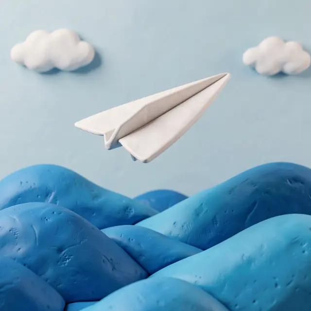 A textured clay paper airplane flies above rolling blue clay hills beneath soft clay clouds on a pale blue sky background.