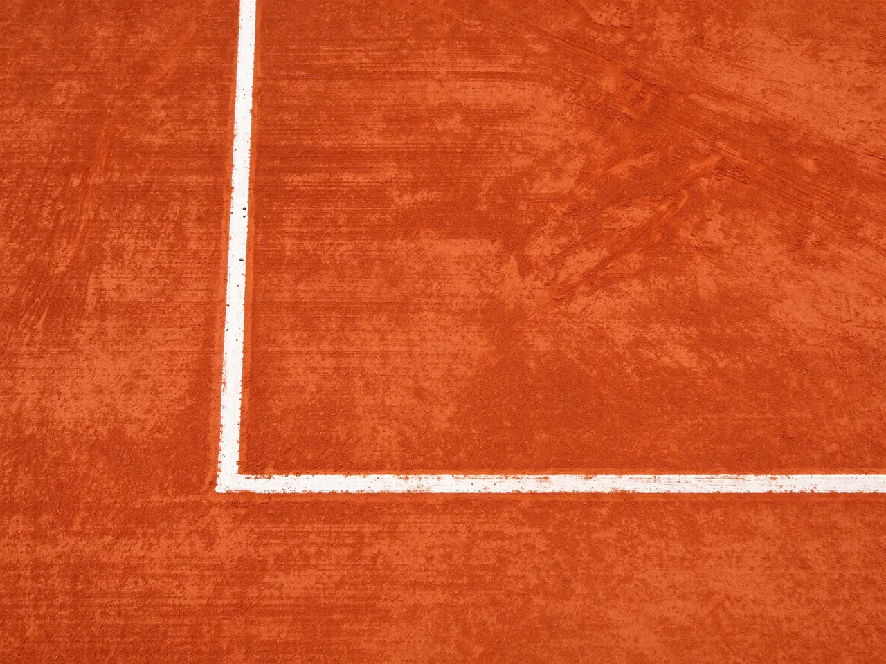 Overhead close-up of the crisp white painted corner lines on a brushed red clay tennis court surface