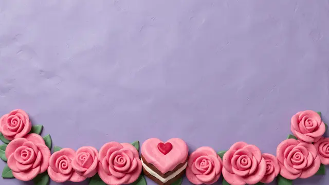 Handmade clay pink roses and a heart-shaped cake line the bottom of a lilac textured background with empty copy space above.