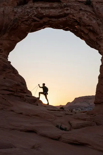 Silhouette of a climber posing inside a natural desert rock arch during warm sunset