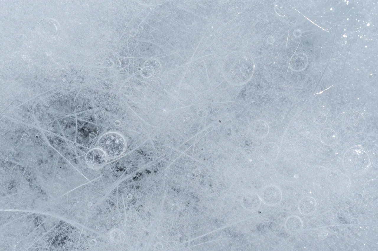 Frosted clear ice surface crisscrossed with fine cracks and dotted with trapped air bubbles
