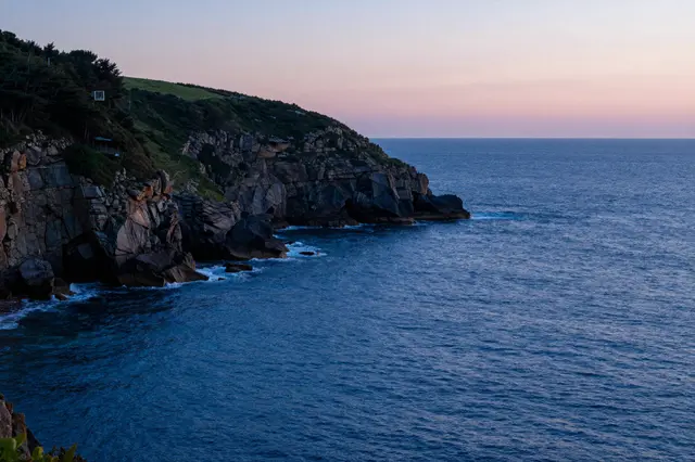 Rocky headland shelters a deep blue sea beneath a soft pink afterglow sky at blue hour