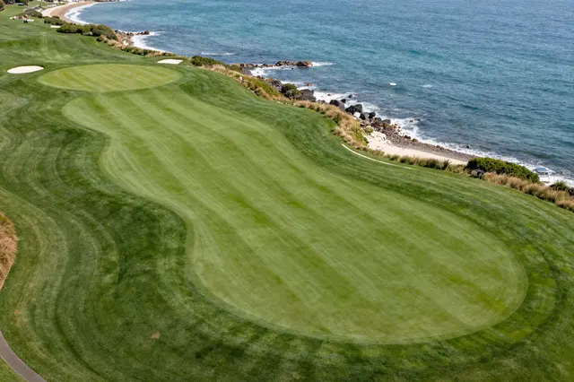 Aerial view of a manicured oceanfront golf hole bordered by rocky shoreline and turquoise sea.