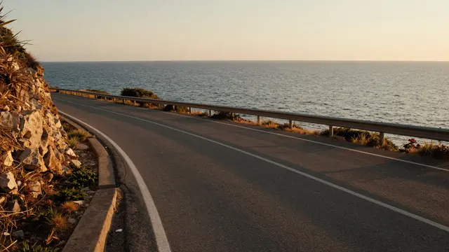 A curving paved coastal road runs alongside the calm sea under warm golden hour light
