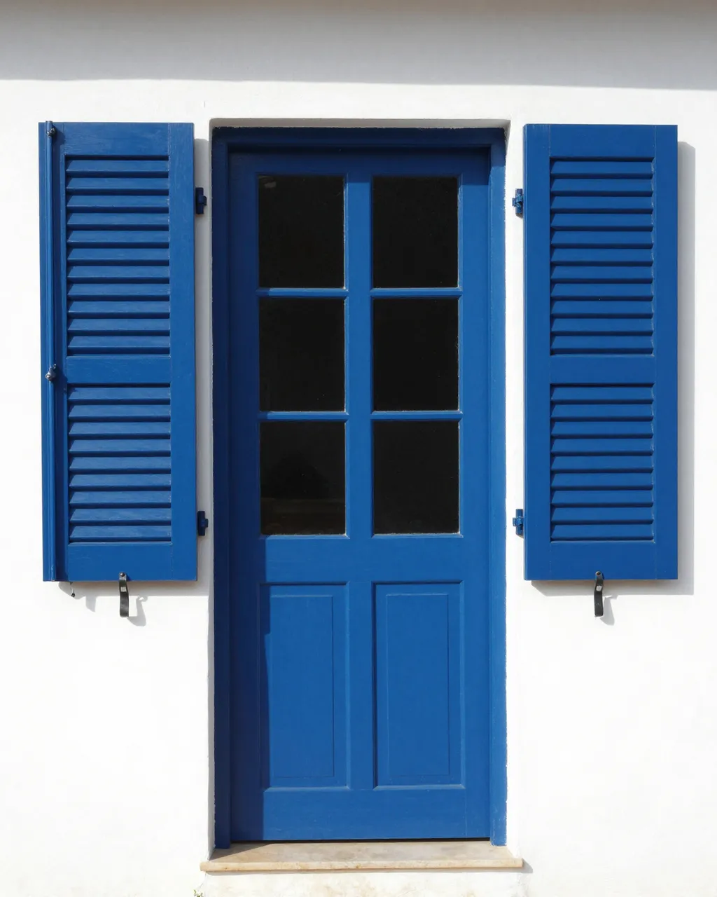 Bright cobalt blue entry door with matching louvered shutters mounted on a sunlit white plaster wall