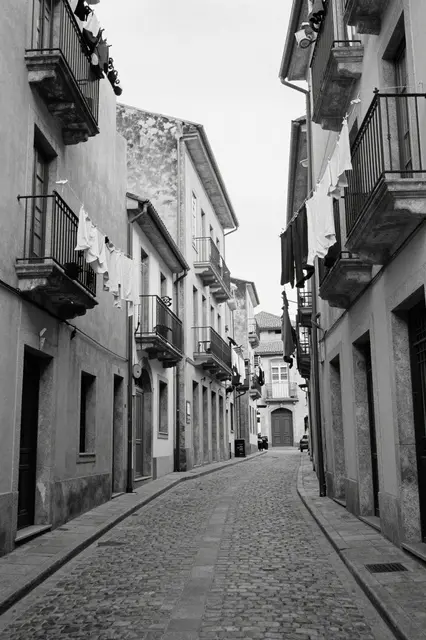 Black and white view of a steep cobbled street lined with old buildings and hanging laundry between balconies
