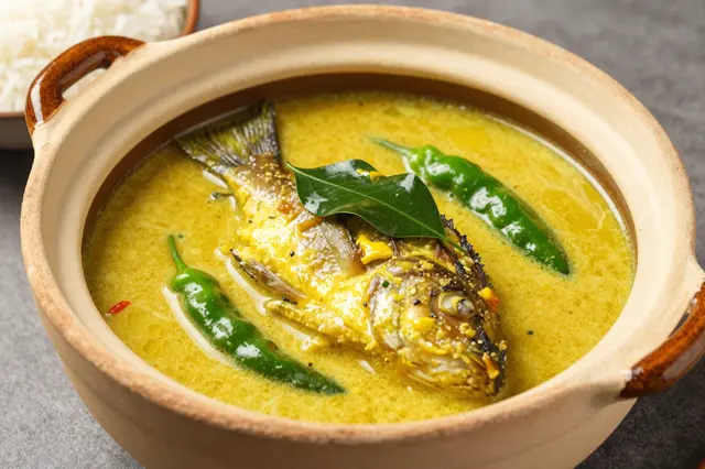 Creamy coconut fish curry with chilies and curry leaf in a clay pot, with rice beside.