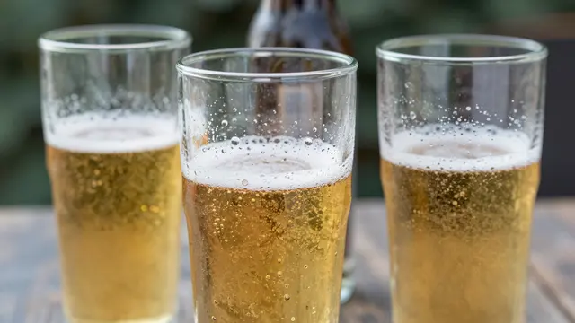 Three frothy cold beer glasses with condensation sit on a wooden outdoor table