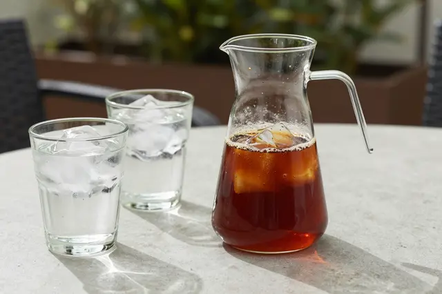 A glass carafe of cold brew coffee sits next to two ice-filled glasses on an outdoor patio table.