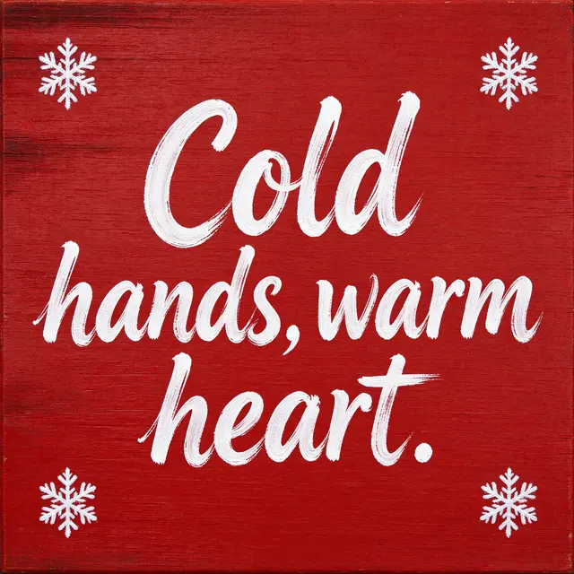 White hand lettering reading "Cold hands, warm heart." sits on a red wooden board with white painted snowflakes in each