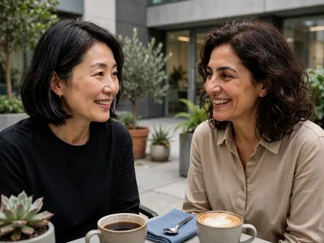Two smiling middle-aged women converse over coffee at an office courtyard table