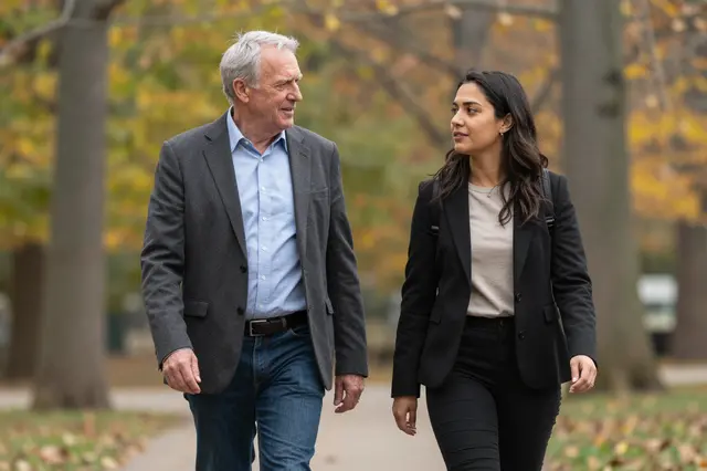 Two business colleagues converse while walking along a paved park path in autumn