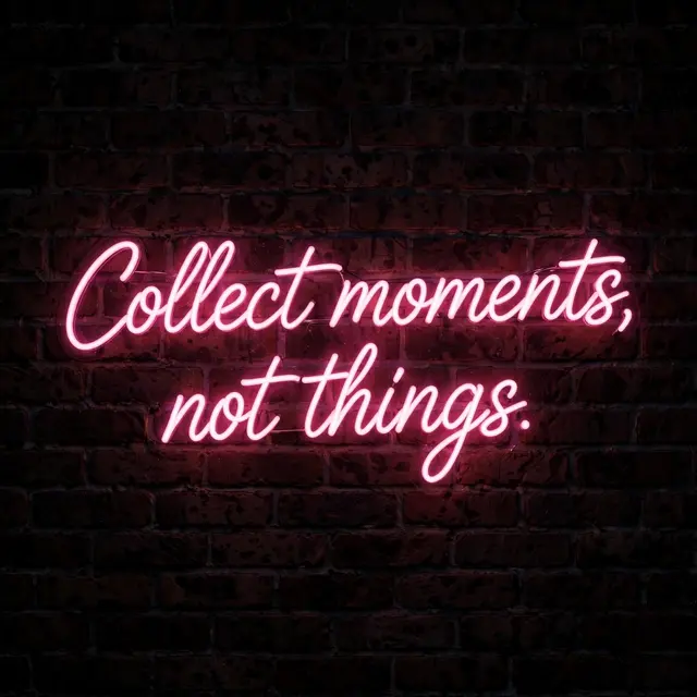 Pink neon script sign reading "Collect moments, not things." glows on a dark brick wall at night