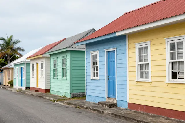 A row of brightly painted wooden houses lines a quiet tropical island street under an overcast sky