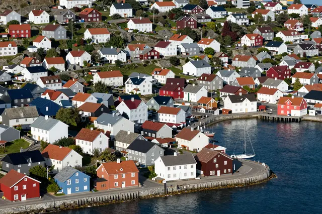Aerial view of a sunlit small harbor town with bright clustered houses wrapping around a calm blue bay