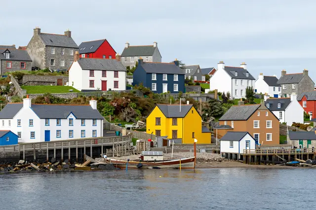 Brightly painted houses line a small sheltered bay with a beached fishing boat under an overcast sky
