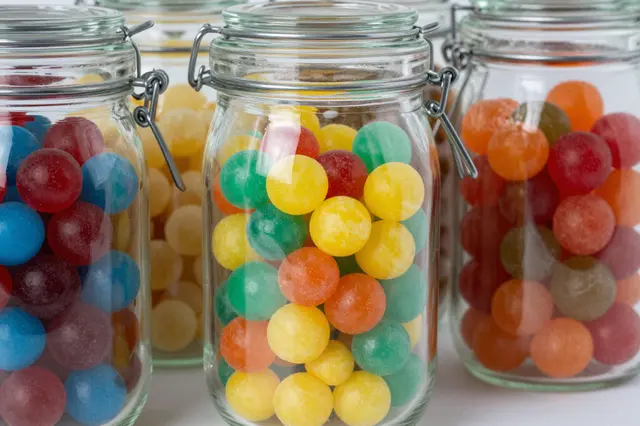 Multiple clear glass clamp jars filled with bright round colorful hard candies arranged in a row on a light surface