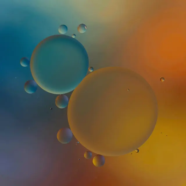Glossy varying size oil droplets float on water over a smooth gradient blue to orange background