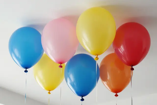 Bright latex balloons in assorted colors float clustered against a plain white indoor ceiling.