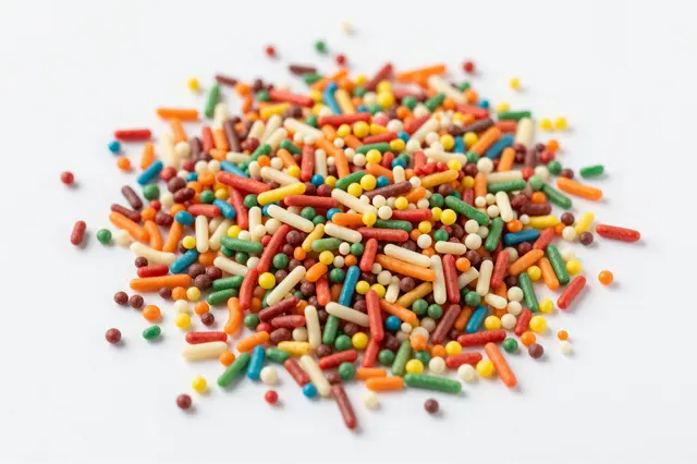 Top-down view of a scattered pile of multicolored rod and round candy sprinkles on a plain white background