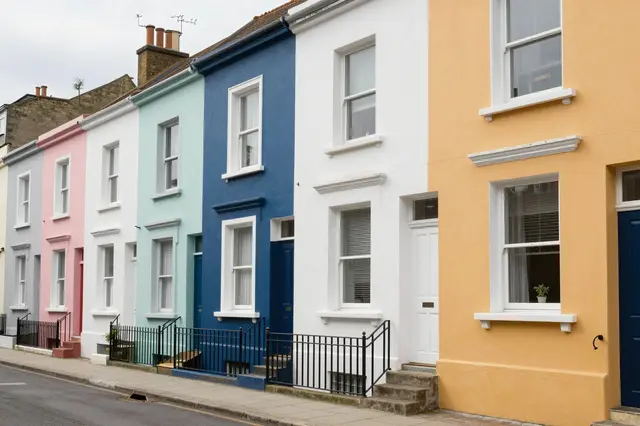 Pastel painted terraced row houses line a gently sloping residential street under an overcast sky