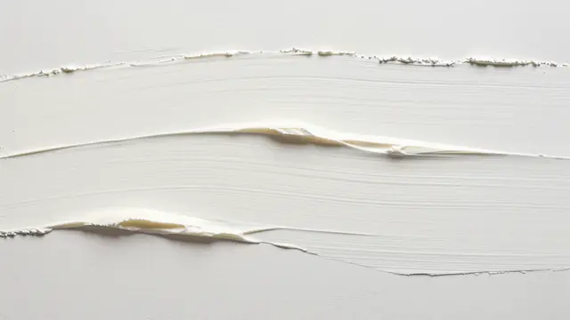 Full frame close-up of cream plaster with long wavy dragged grooves under flat even light