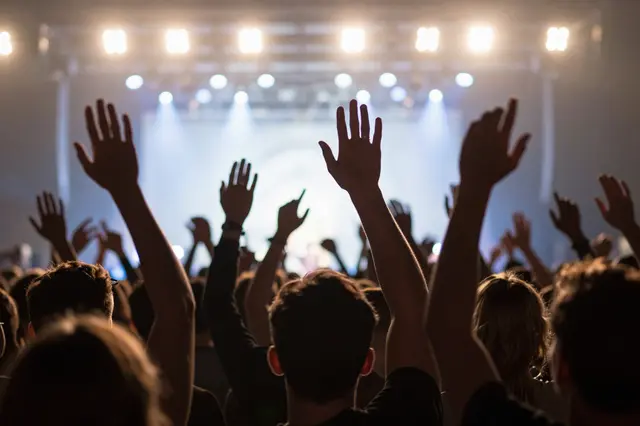 Rear view of a concert audience with raised hands lit by bright overhead stage lights