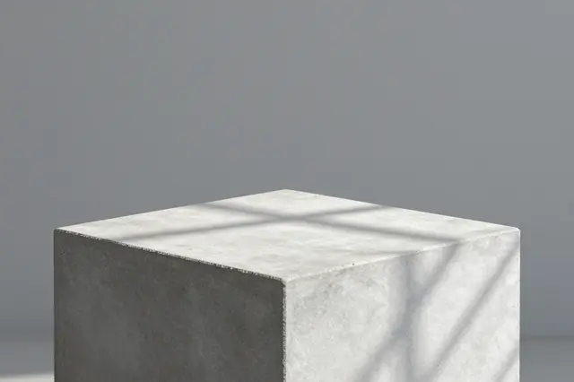 A raw concrete cube podium sits against a muted gray backdrop with soft window shadow patterns