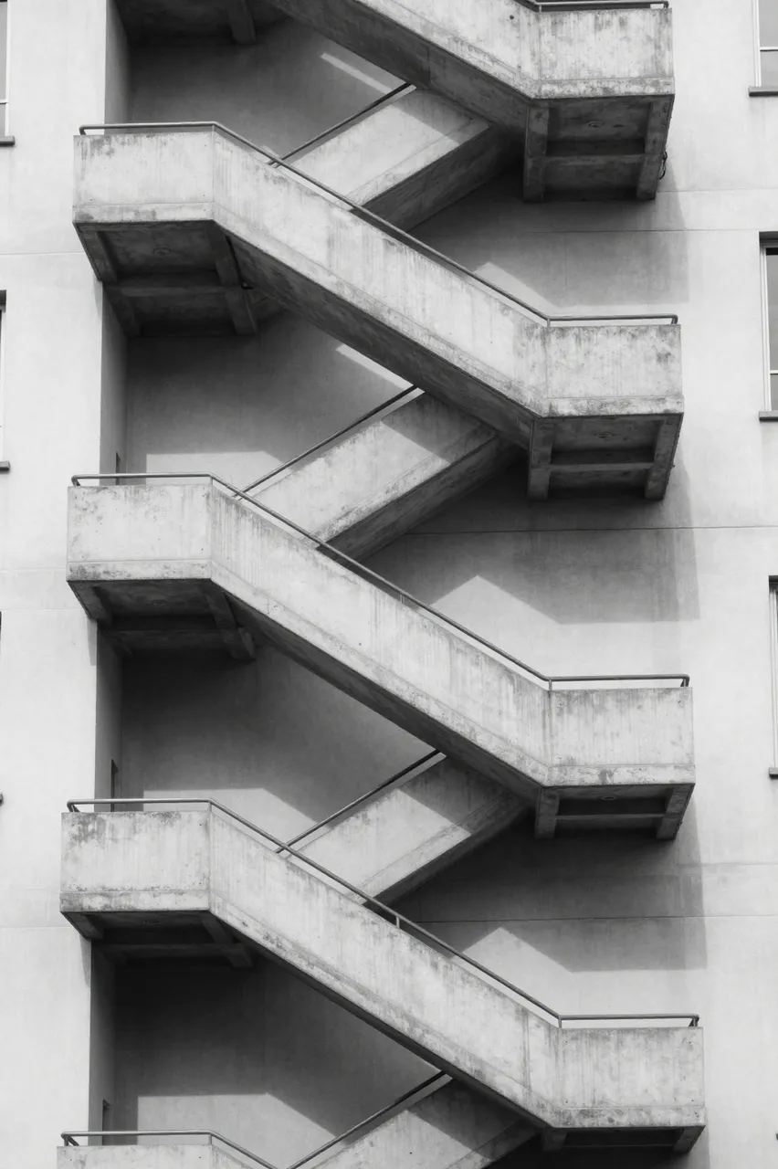 Black and white close-up of a zigzagging external concrete staircase on an apartment building in sharp noon light