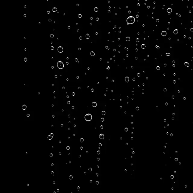 Scattered fine and larger clear water droplets against a solid pure black background