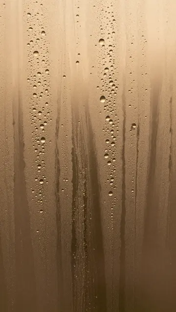 Close-up of water droplets and streaky condensation on glass lit by warm amber light behind