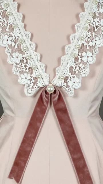 Close-up of a blush pink dress neckline trimmed with white lace, pearl accents and a velvet ribbon bow