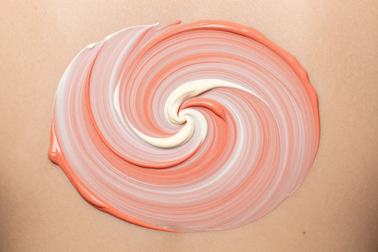 A tight circular swirl of wet coral and cream acrylic paint sits on a light tan flat surface under even lighting