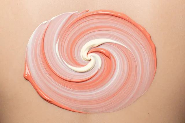A tight circular swirl of wet coral and cream acrylic paint sits on a light tan flat surface under even lighting