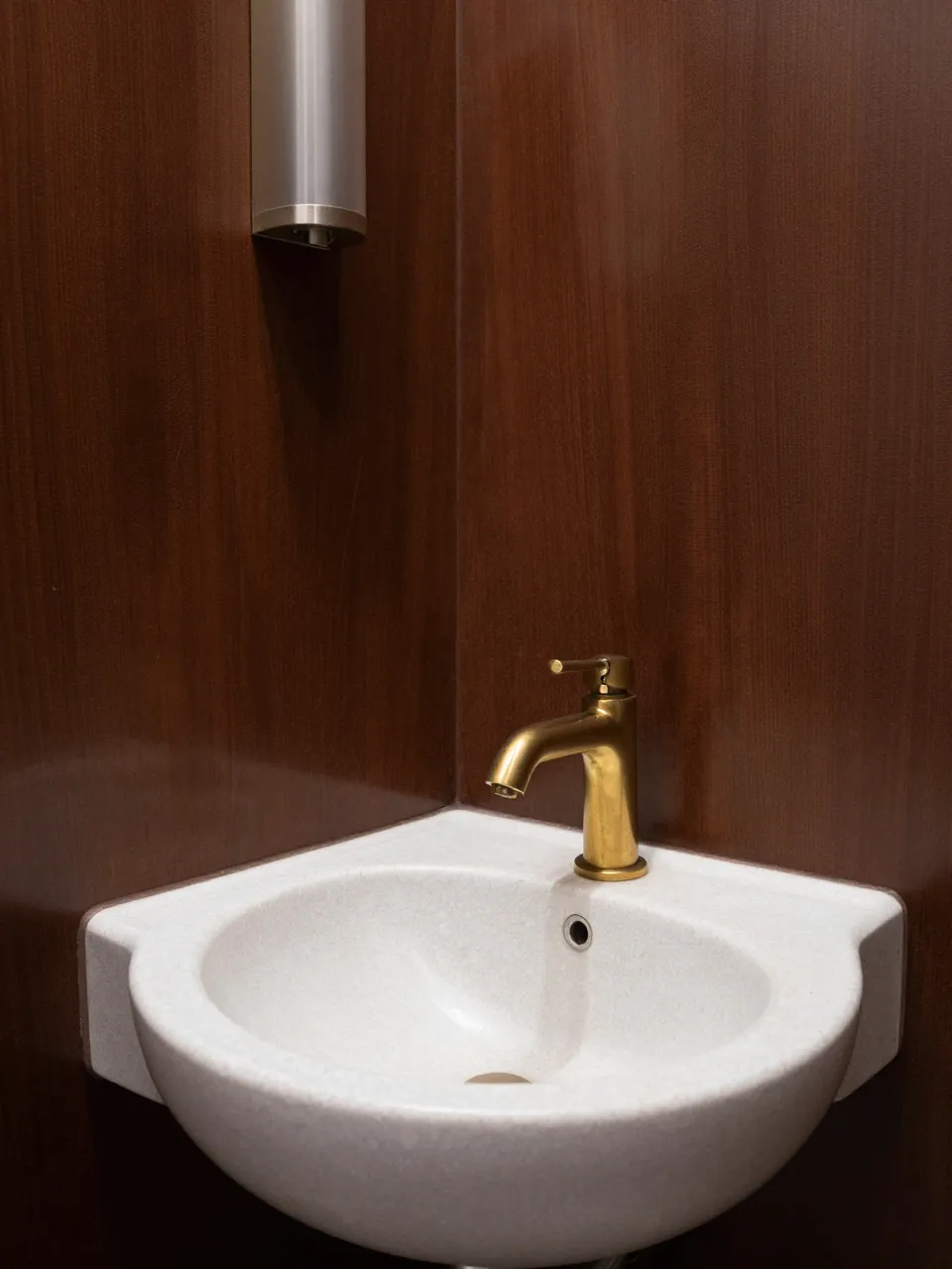 Wall-mounted travertine corner sink with brass faucet against dark brown lacquered walls