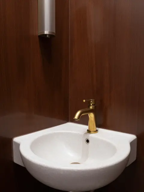 Wall-mounted travertine corner sink with brass faucet against dark brown lacquered walls